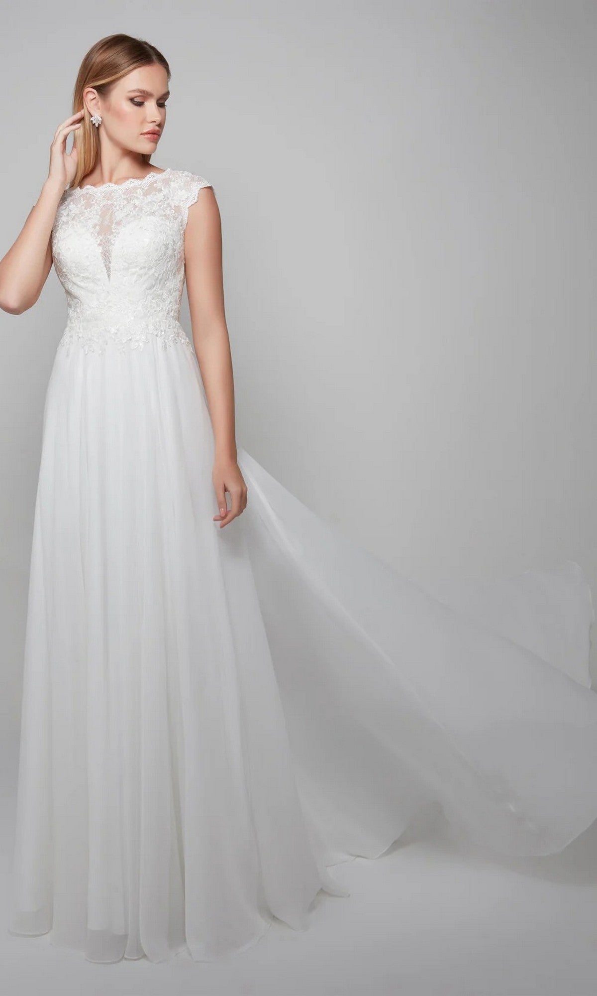 A woman wearing the Alyce 7073 Long White Dress, featuring a sleeveless lace-embroidered bodice and flowing chiffon A-line skirt, stands against a plain light background.